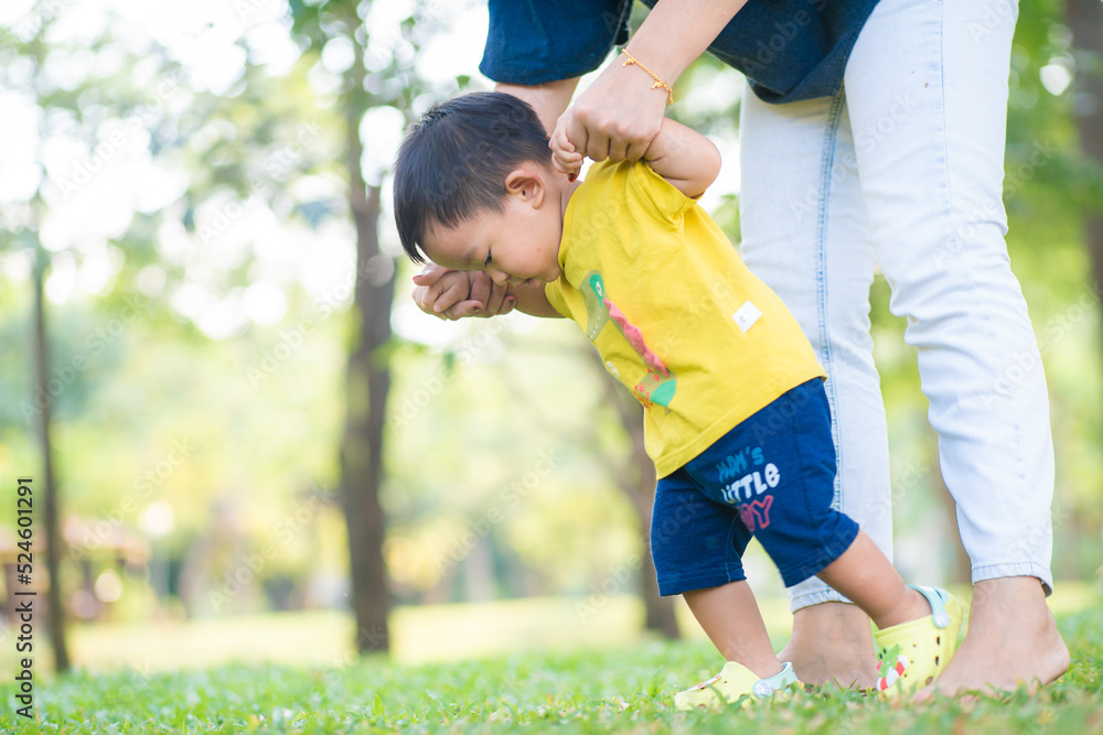 Obraz premium Toddler asian boy practice walking on green grass park with mom