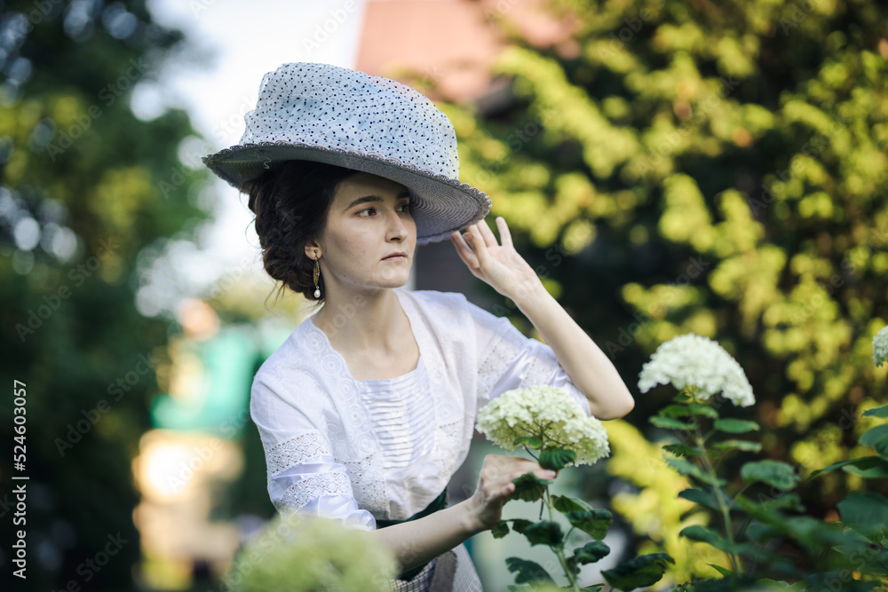 Portrait of a young slender woman in a 1910s costume. A lady in a hat in the fashion of the early 20th century walks in a garden