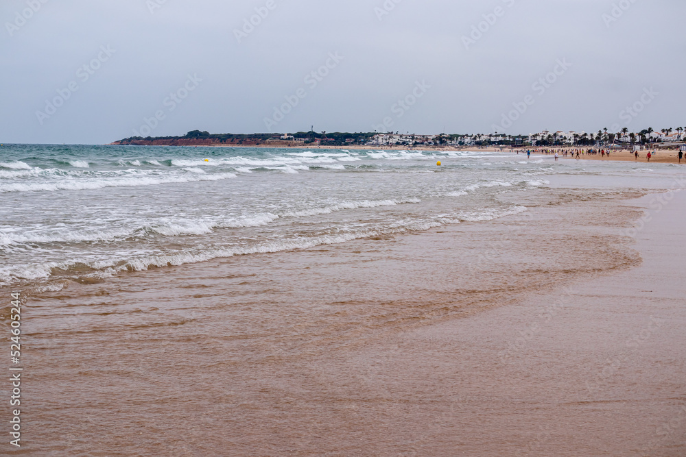 Fototapeta premium people walking along the seashore, early in the morning, at La Barrosa beach in Sancti Petri, Cadiz, Spain