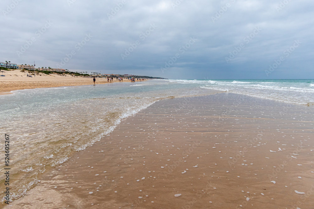 people walking along the seashore, early in the morning, at La Barrosa beach in Sancti Petri, Cadiz, Spain