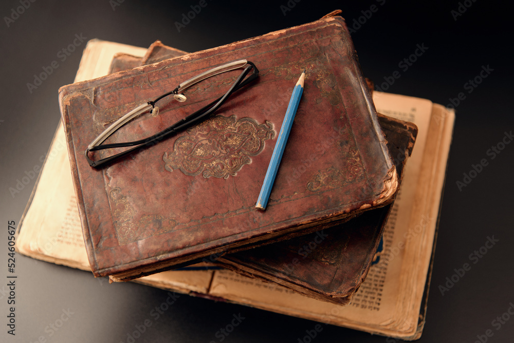 Stack of old worn jewish leather cover books on open Torah page on dark background. Closeup. Selective focus.