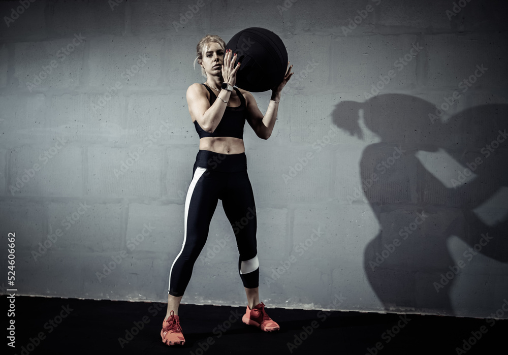 Sportswoman doing stretching exercise with medicine ball. Muscular woman exercising fitness ball at gym Sportswoman doing stretching exercise with medicine ball. Muscular woman exercising fitness ball at gym