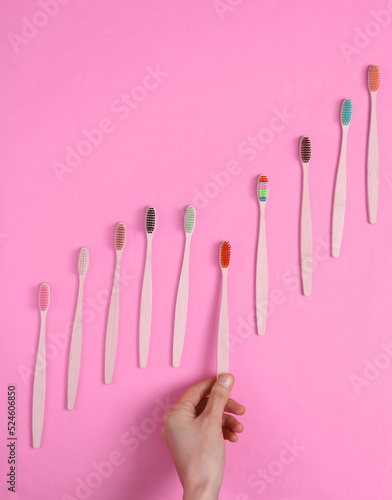 Hand selects Eco-friendly bamboo toothbrush among the set on pink background