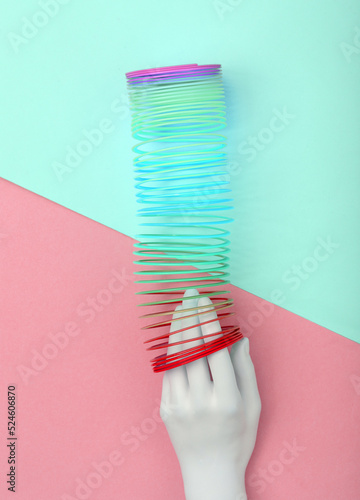 White hand and Rainbow plastic multicolored spiral slinky toy on pink  blue background. Minimalism photo
