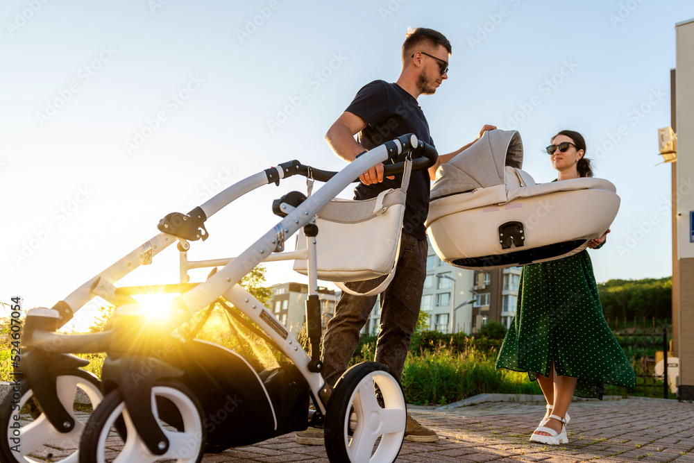 A young family on a walk with a baby in a stroller. A woman holds a cradle in her hands while a man lays out a stroller