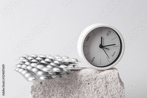 Round Clock with pills blister on stone, gray background. Minimal composition photo