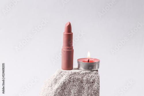 Natural cosmetic. Beauty products. Lipstick tube with candle on stone podium, gray background. Product photo. Abstract composition. Natural showcase photo