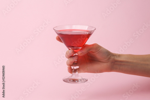 Party concept. Hand holding cocktail glass on pink background
