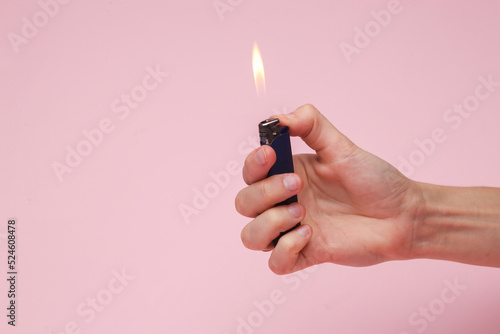 Hand holding a lighter with a flame on a pink background photo