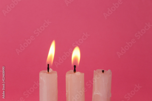 Flaming wax candle on a pink background