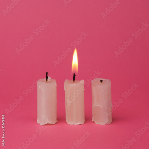 Flaming wax candle on a pink background