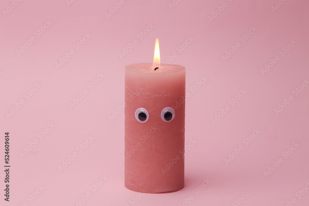 Flaming candle with eyes on pink background Flaming candle with eyes on pink background