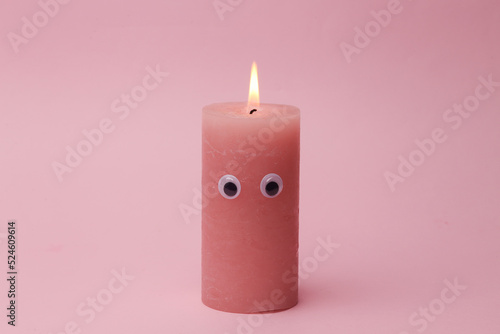 Flaming candle with eyes on pink background