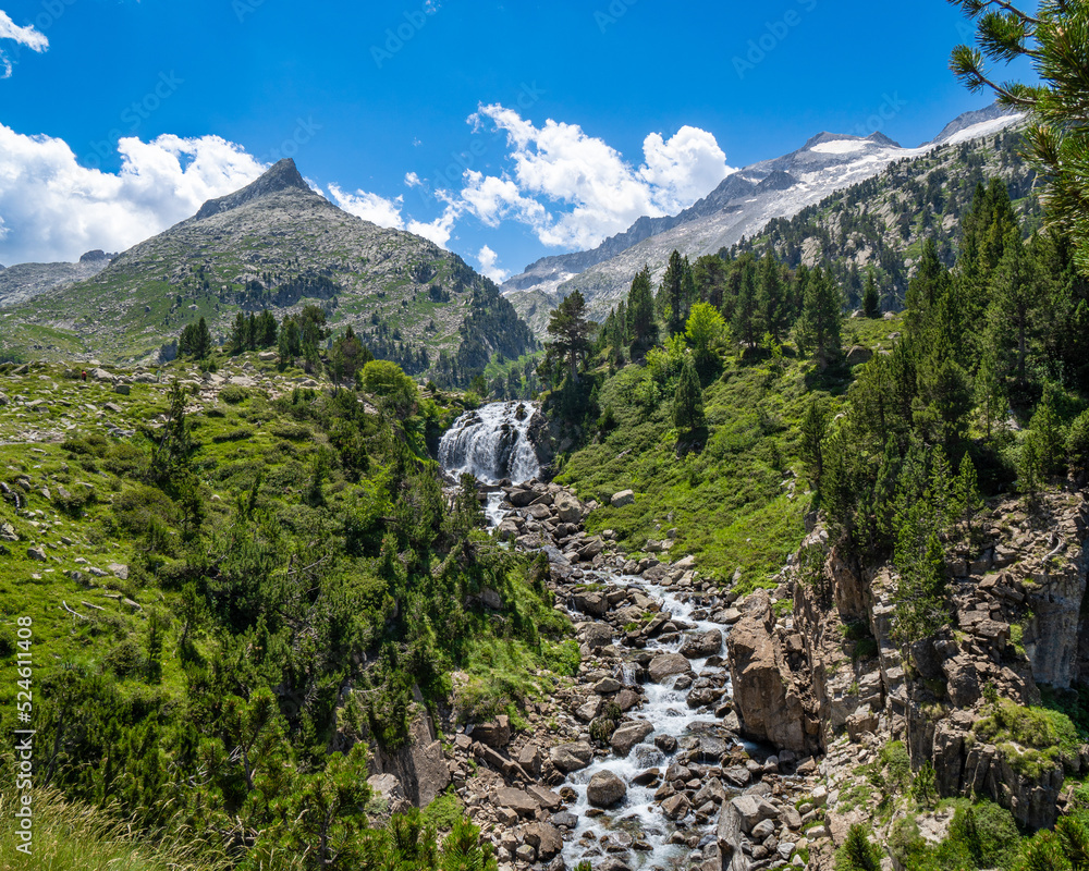 Spectacular river with large stones coming down from a waterfall in the Aragonese Pyrenees of Benasque. Mountains and clouds in the background.