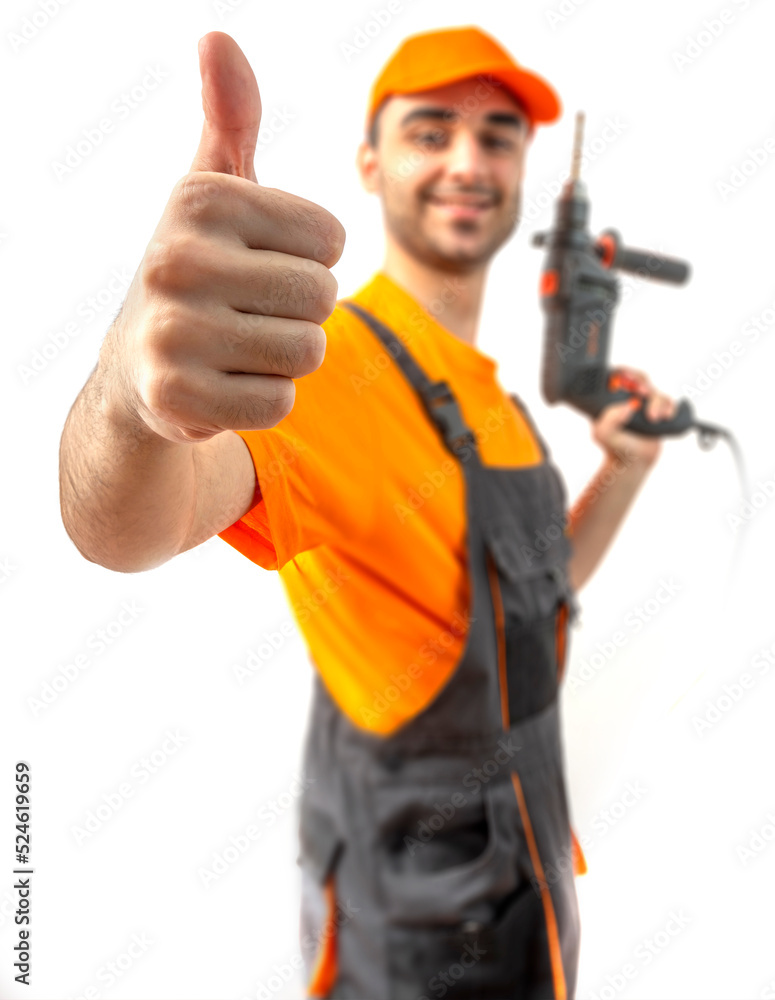 Young worker drilling with electric drill in his hands. Tool for boring holes. Craftsman repairman wearing orange uniform cap and t-shirt, overalls on a white isolated background for advertising Young worker drilling with electric drill in his hands. Tool for boring holes. Craftsman repairman wearing orange uniform cap and t-shirt, overalls on a white isolated background for advertising