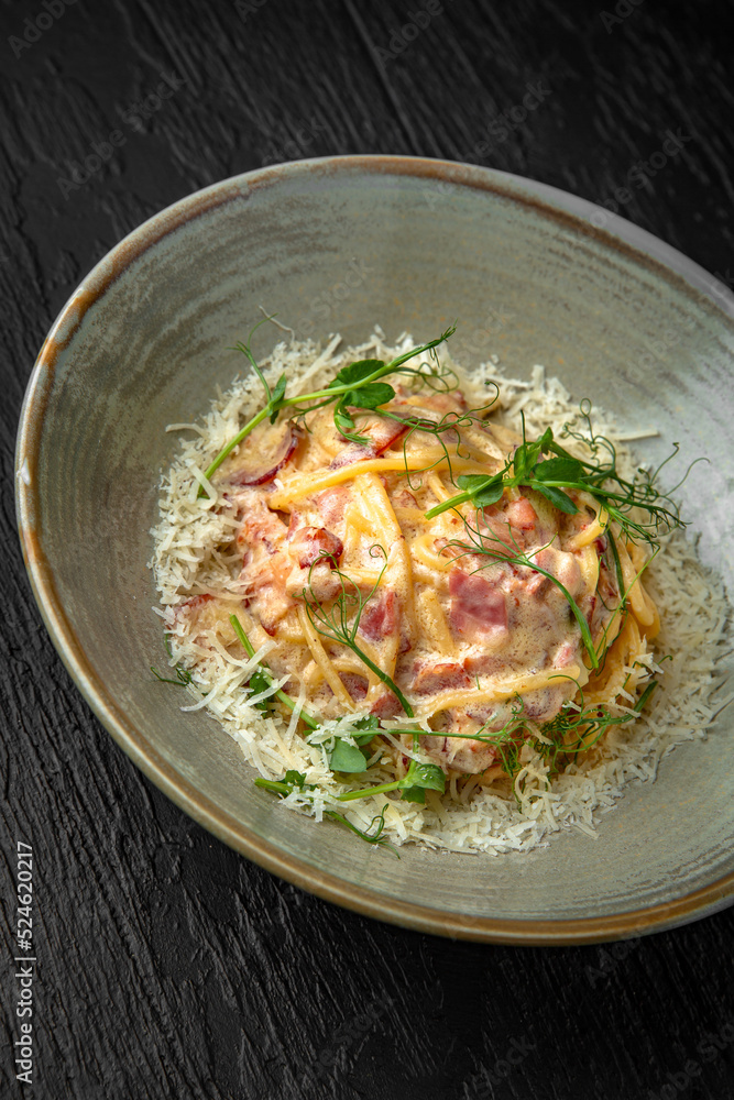 Delicious pasta carbonara with ham and cheese in a ceramic plate on a dark textured background. Restaurant menu Isolated on black Delicious pasta carbonara with ham and cheese in a ceramic plate on a dark textured background. Restaurant menu Isolated on black