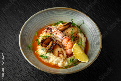 Delicate risotto with champagne and seafood: langoustines, mussels, squids in a ceramic plate on a dark textured background. Restaurant menu Isolated on black