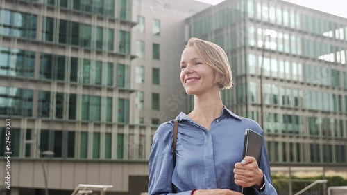 Confident business woman walking in outdoors office city carrying laptop. Elegant blond female executive enjoying successful corporate career photo