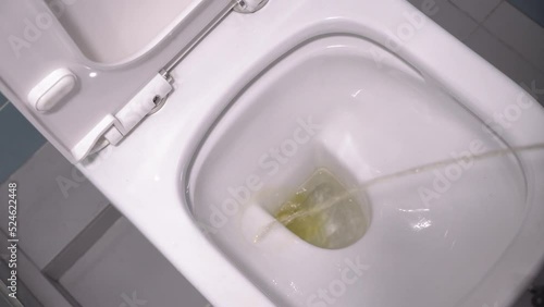 Person stands in modern toilet, and pees in first person. stream of urine flies directly into opening of toilet. Then he pours everything with clean water. Modern renovation of toilet room. photo