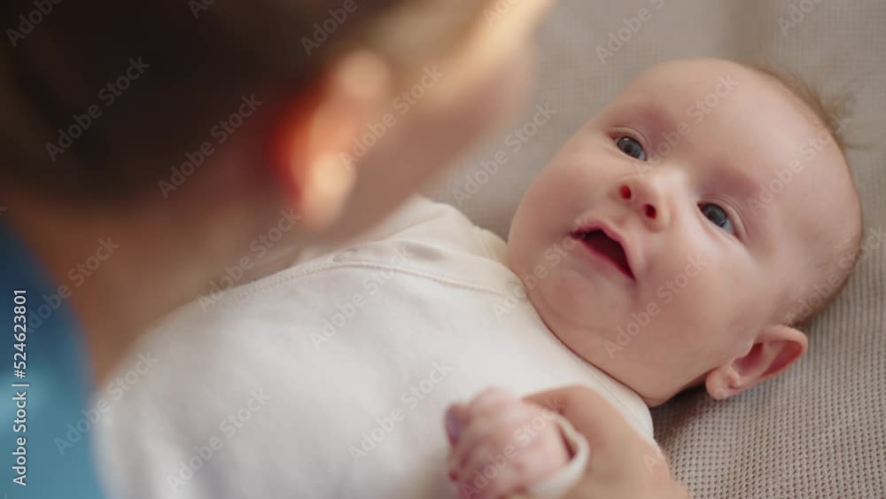 Happy mom spends time with her baby. Mother playing and kissing with a newborn baby.  Face of an active baby looking at a parent.  Mama is  kissing her infant. motherhood and family concept.