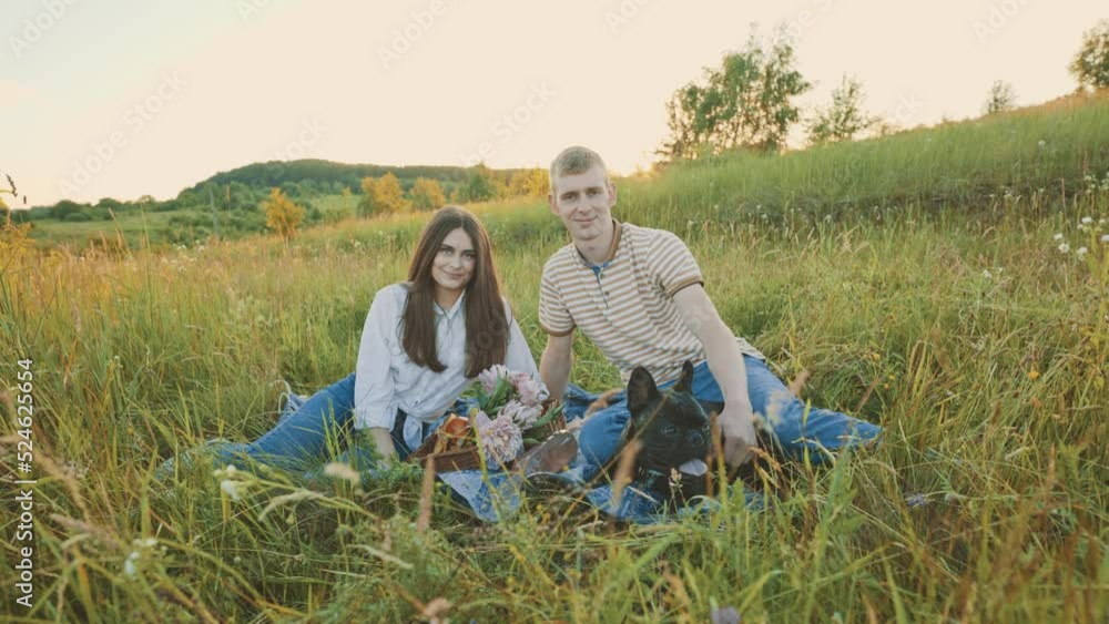 young happy couple having picnic with their french bulldog outdoors in the countryside during beautiful sunset. Romantic date near the lake young happy couple having picnic with their french bulldog outdoors in the countryside during beautiful sunset. Romantic date near the lake