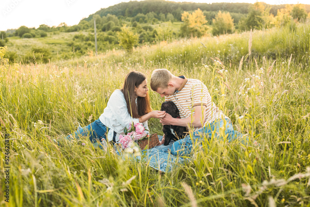 young happy couple having picnic with their french bulldog outdoors in the countryside during beautiful sunset. Romantic date near the lake young happy couple having picnic with their french bulldog outdoors in the countryside during beautiful sunset. Romantic date near the lake