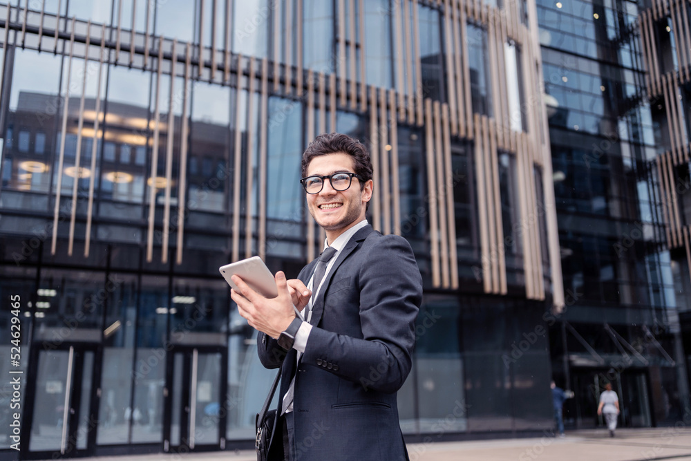 Fototapeta premium A male employee of a financial company, goes to work in an office in a business suit, uses a tablet and writes a message