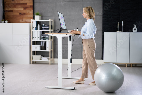 Fotografija Woman Using Adjustable Height Standing Desk In Office