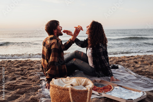 Woman and man eating pizza by the sea, young couple having a picnic and meeting dawn on the beach