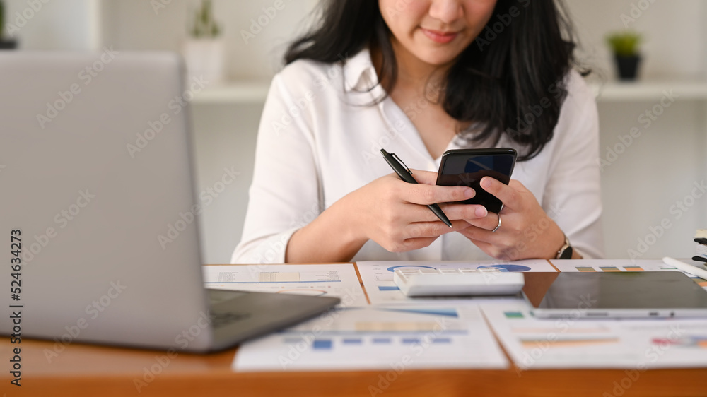 Female office worker sitting front of laptop and chatting online on smart phone Female office worker sitting front of laptop and chatting online on smart phone