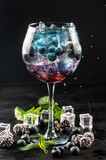 Colored blue and red cocktail with blueberry and ice on black background