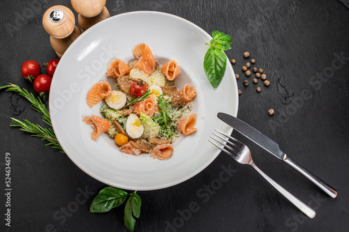 Dish of salmon with eggs, herbs and salad on wooden background