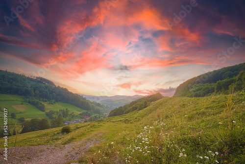 beautiful sunrise in the mountain area. the sky plays with warm colors. hills with fields and forests. countryside. summer season. Breathtaking nature scenery during sunset.  © robertuzhbt89