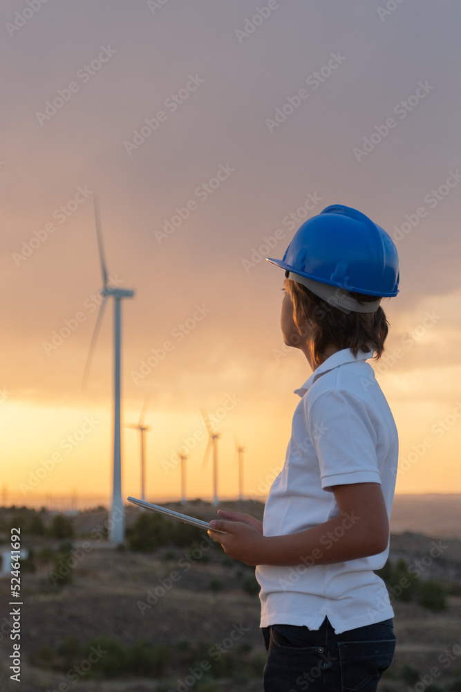 child and turbine. Engineer working on a wind farm at sunset. He watches the operating data of the windmills on his tablet. Renewable energies.