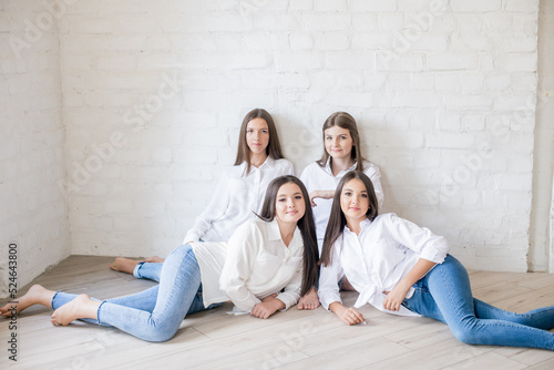  Pretty teenage girls models in trendy jeans and white shirts in the studio against the background of a white brick wall. Teenage fashion. beauty and fashion
