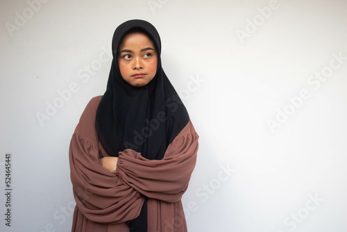Serious young Asian Muslim woman crossing hands makes annoyed gesture and demonstrates confusing isolated over white background