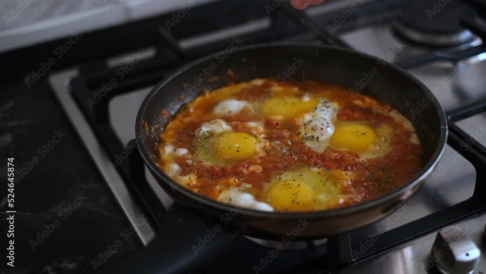 woman sprinkles shakshuka with spices close-up. scrambled eggs with vegetables in a frying pan close-up woman sprinkles shakshuka with spices close-up. scrambled eggs with vegetables in a frying pan close-up