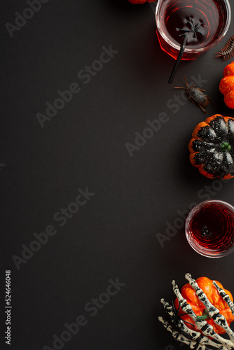 Fototapeta Naklejka Na Ścianę i Meble -  Halloween concept. Top view vertical photo of drink in glasses with floating spiders and straw skeleton hand holding pumpkin centipede and cockroach on isolated black background with copyspace