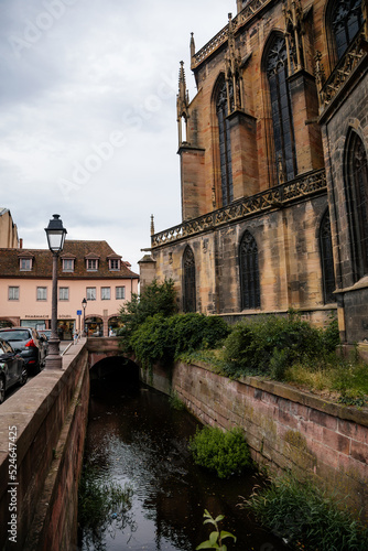 Colmar, Alsace, France, 4 July 2022: town capital of Alsatian wine, narrow picturesque street with medieval colorful houses, Roman Catholic Gothic St Martins Church with tower at summer day