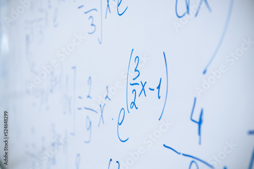 Physical and mathematical formulas written with a blue marker on a white board in a high school classroom. Abstract background close-up