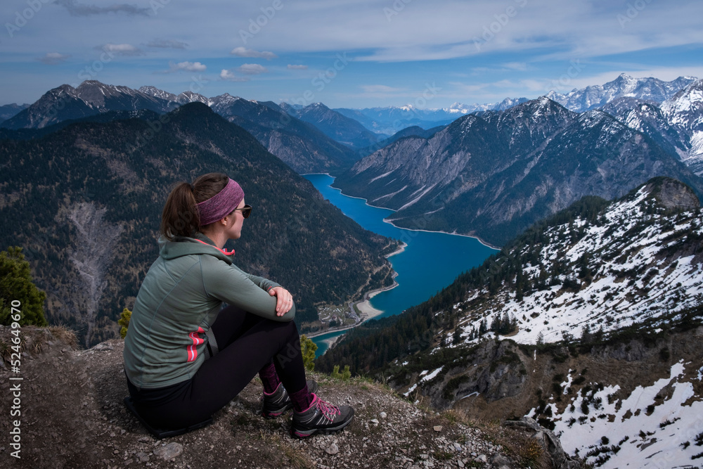 Hiking woman sitting on summit of Zunterkopf with view at Lake Plansee with mountains in Tyrol Austria during sunny weather.