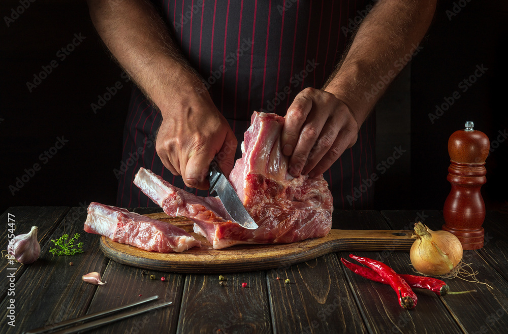 The chef cuts raw meat ribs on a cutting board before baking. Cooking delicious food in the kitchen. Delicious grill idea