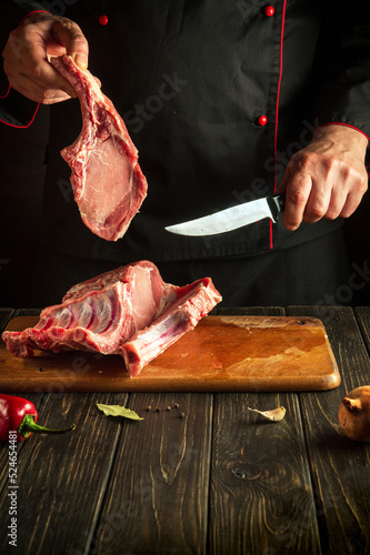 The chef cuts raw ribs on kitchen wooden cutting board. Barbecue grill idea.