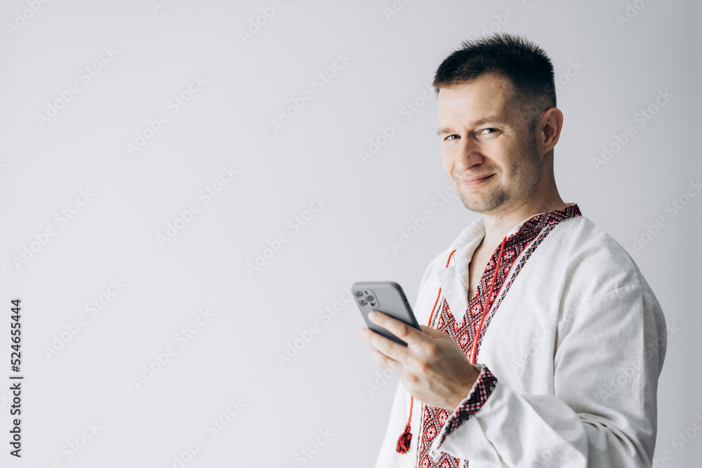 Guy in Ukrainian vyshyvanka stands holding phone, takes selfie and smiles. Guy in Ukrainian vyshyvanka stands holding phone, takes selfie and smiles.
