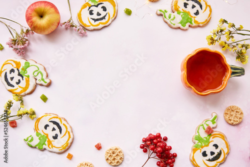 Halloween creative concept background: pumpkin cup and cookies in shape of cute pumpkins. Copy space.Atmospheric aesthetic autumn mood or trick or treat concept. Apples, dry flowers and candied fruit