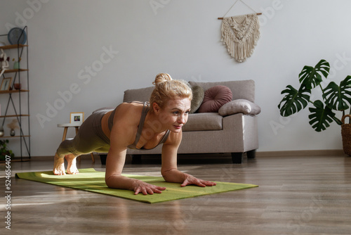 Sporty adult woman practicing yoga in the comfort of her own home. Fit middle aged yogini performing forearm plank exercise at the living room. Interior background, copy space, close up.