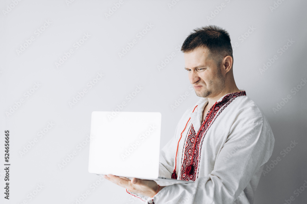 Guy in Ukrainian vyshyvanka stands holding laptop. Guy in Ukrainian vyshyvanka stands holding laptop.