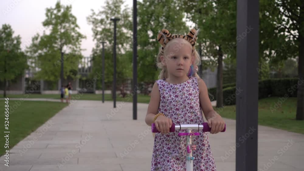 Child girl rides a scooter outdoors. Happy girl riding a scooter in the park Child girl rides a scooter outdoors. Happy girl riding a scooter in the park