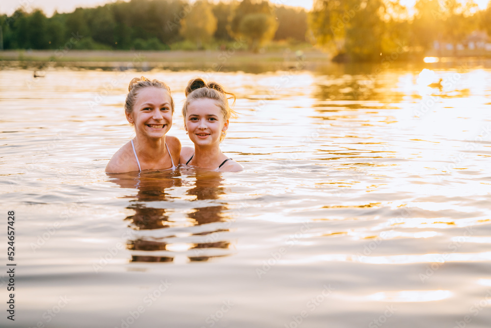 Two teenager girls friends are bathing and looking at the camera enjoying vacation in summer season in sunset.