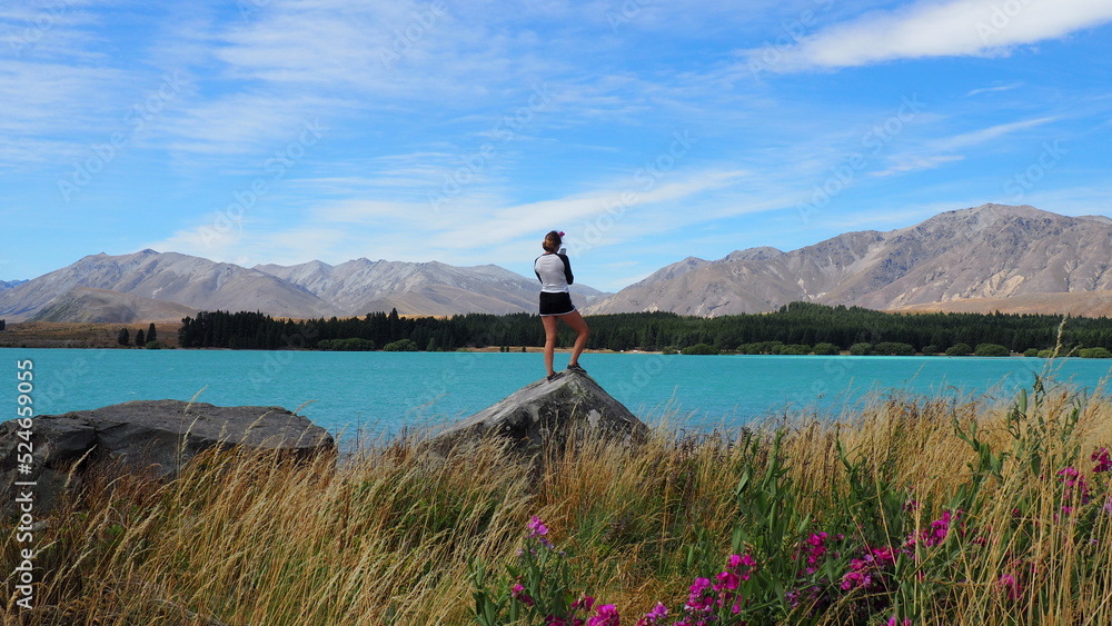 Lake Tekapo. Tekapo, New Zealand.

Young lady standing on a rock admiring the beautiful view of Lake Tekapo and surrounding mountain ranges.